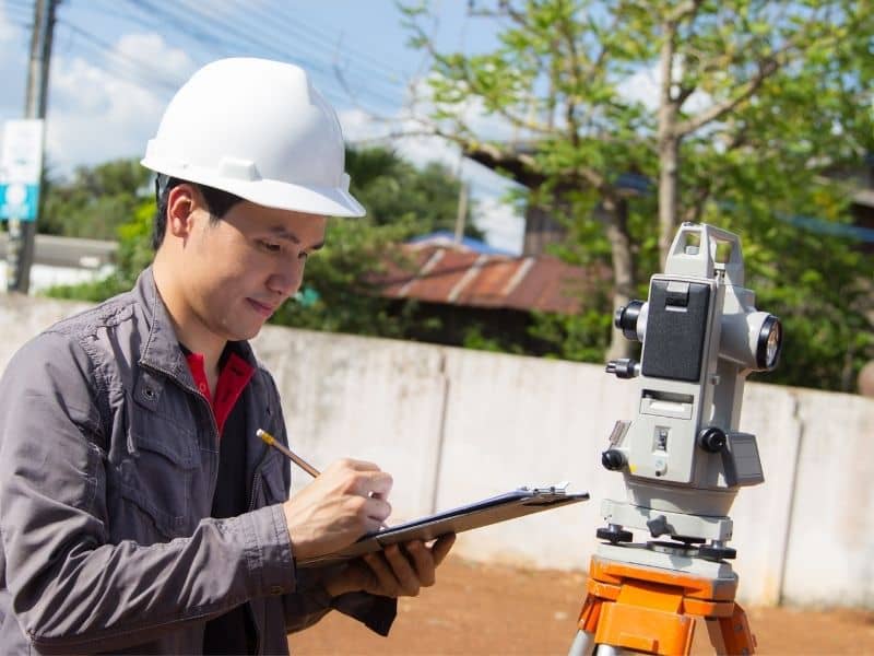 Land surveyor recording measurements beside total station equipment to verify historic parcel boundaries using modern surveying methods.