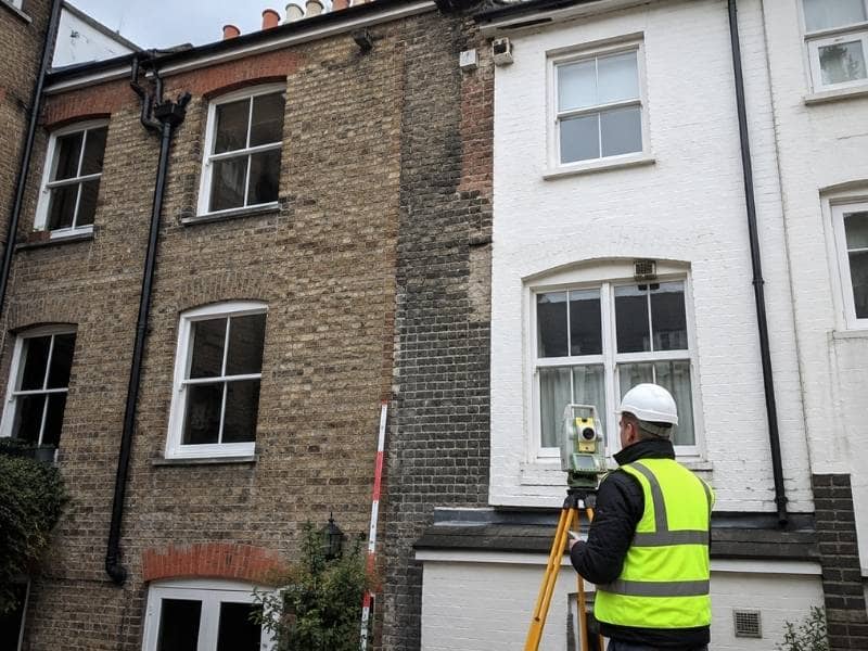Surveyor measuring the shared masonry wall between adjoining buildings before structural renovation